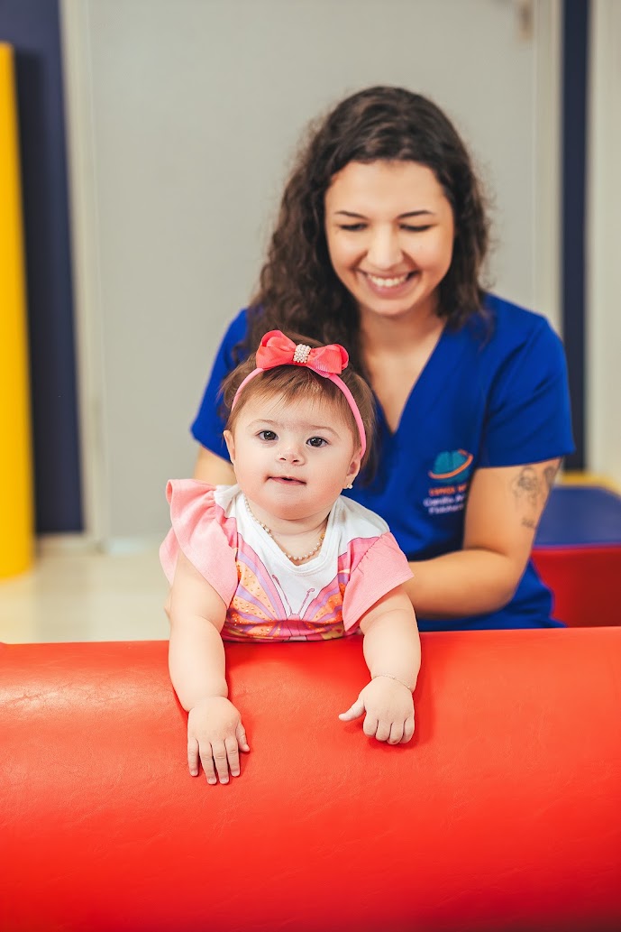 Fisioterapeuta acompanhando bebê em atividade sobre rolo terapêutico